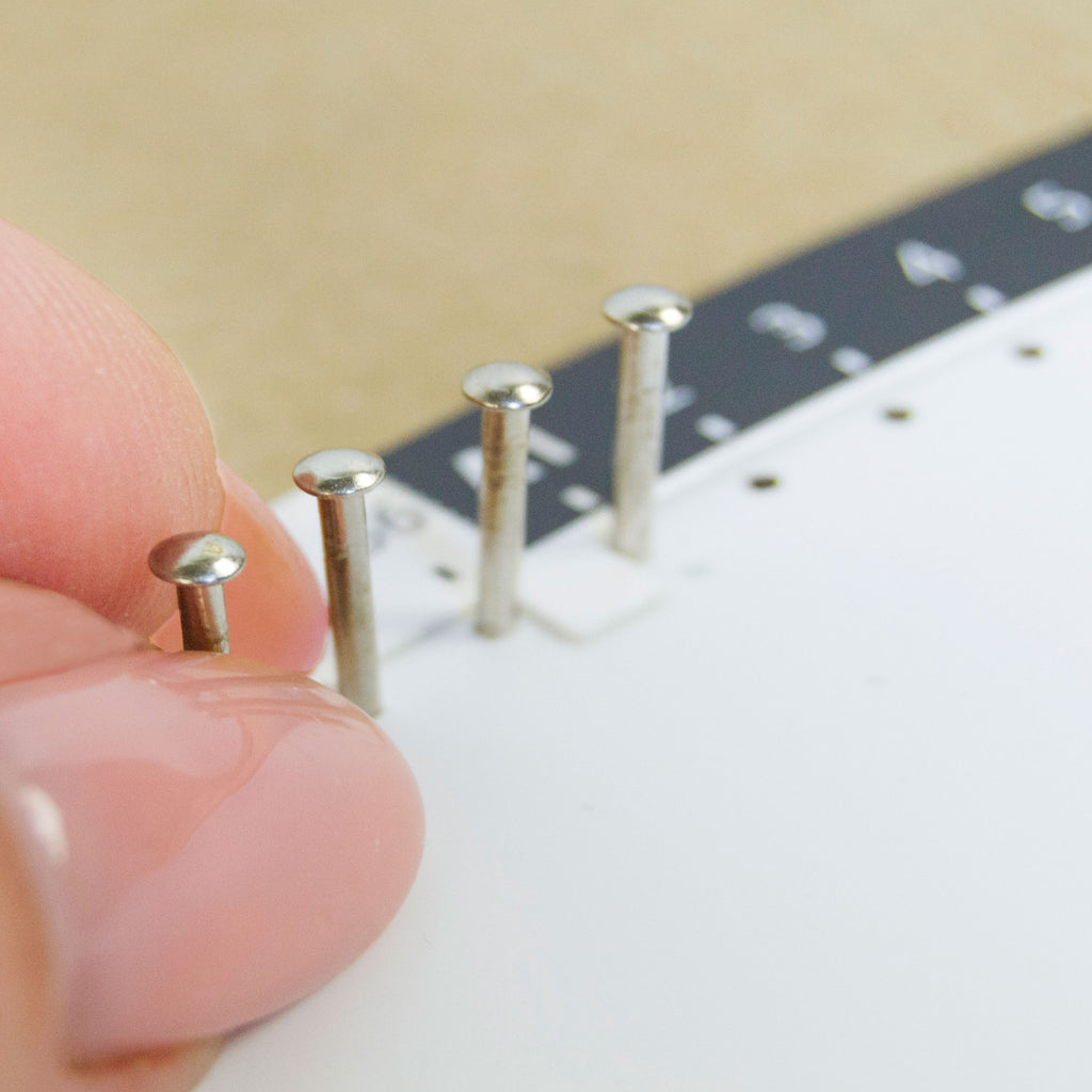 Placing metal nails into a pre-marked circular string art base during assembly