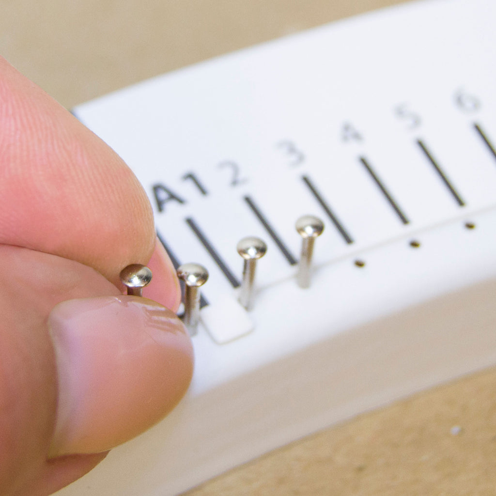 Placing metal nails into a pre-marked string art base following the numbered guide