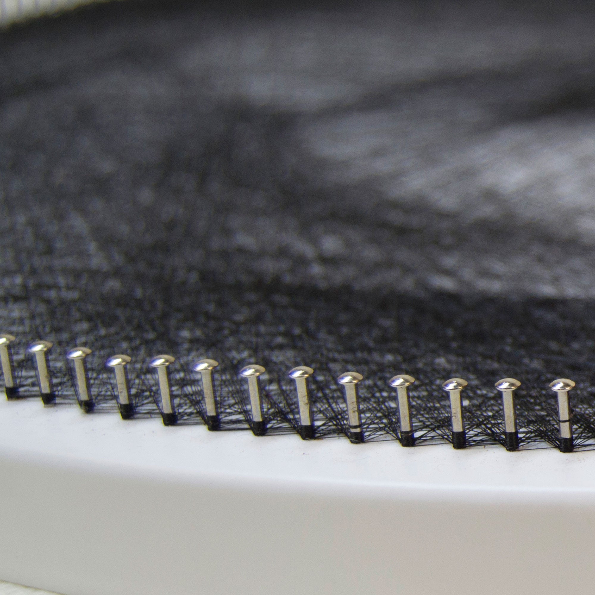 Close-up of metal nails and black thread forming a dense string art pattern on a circular base